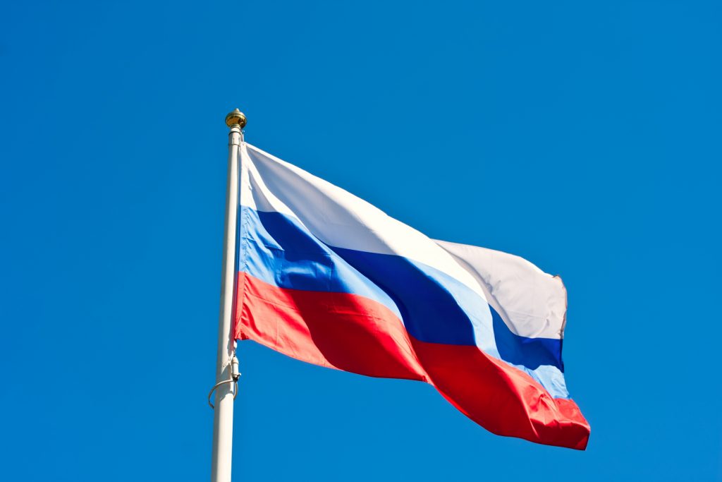 Bilden består av Rysslands flagga. Bilden är tagen underifrån mot en blå himmel.