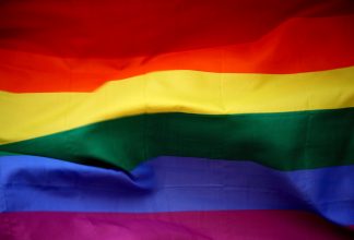The picture consists of the pride flag with the colours red, yellow, green, blue and purple in stripes. It is a close-up picture.