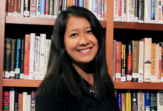 Esther Htu San står framför en stor bokhylla fylld av böcker och ler.