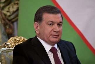 Uzbekistans president Shavkat Mirziyoev på en stol. Flagga i bakgrunden.