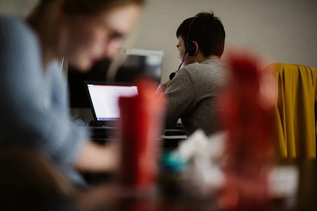 A man in front of a laptop wearing a headset.