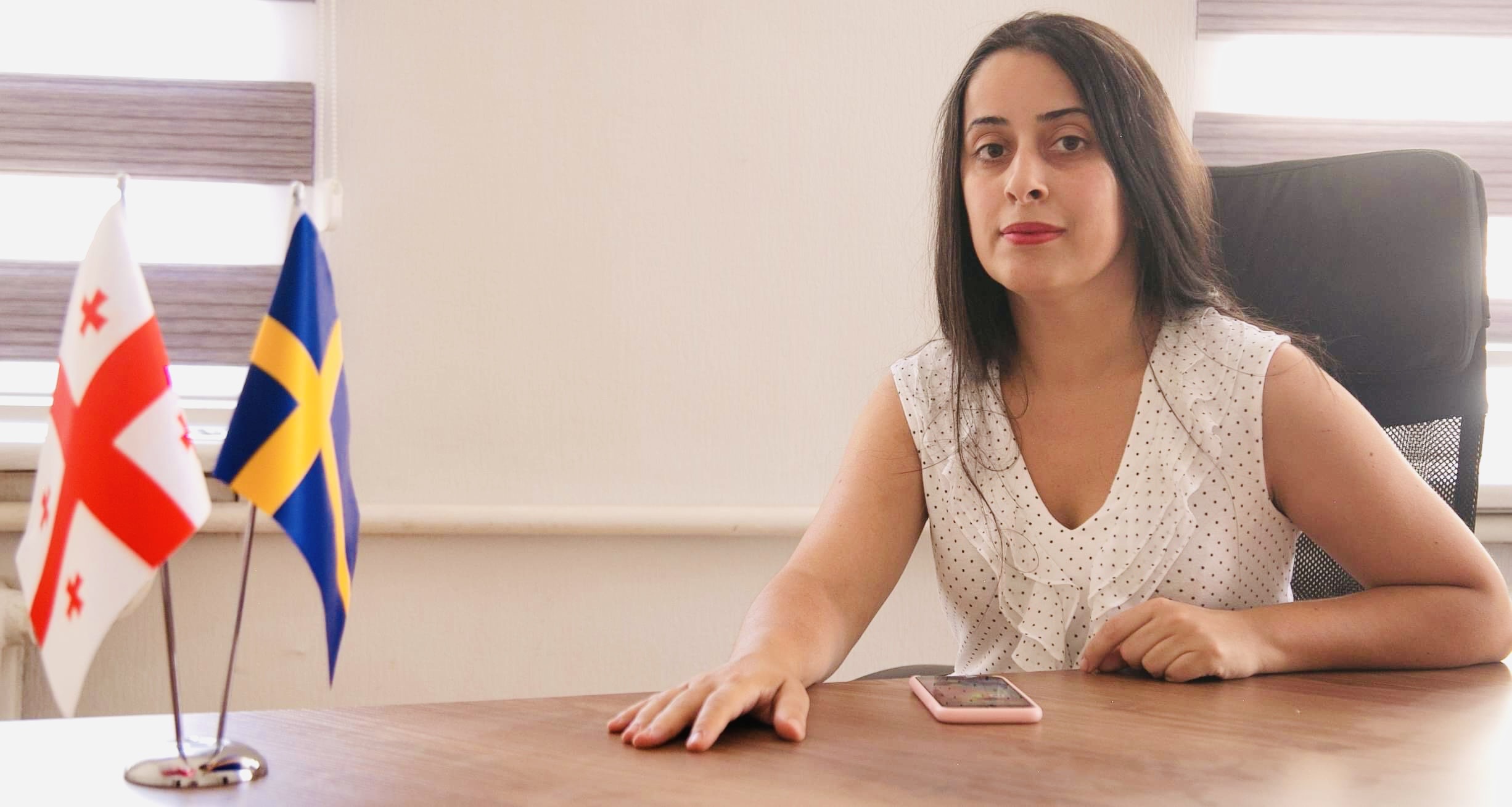 A woman sitting by a desk with a Georgian and a Swedish flag. 