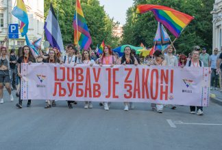 People waving Pride flags and walking behind a banner at Pride in Sarajevo