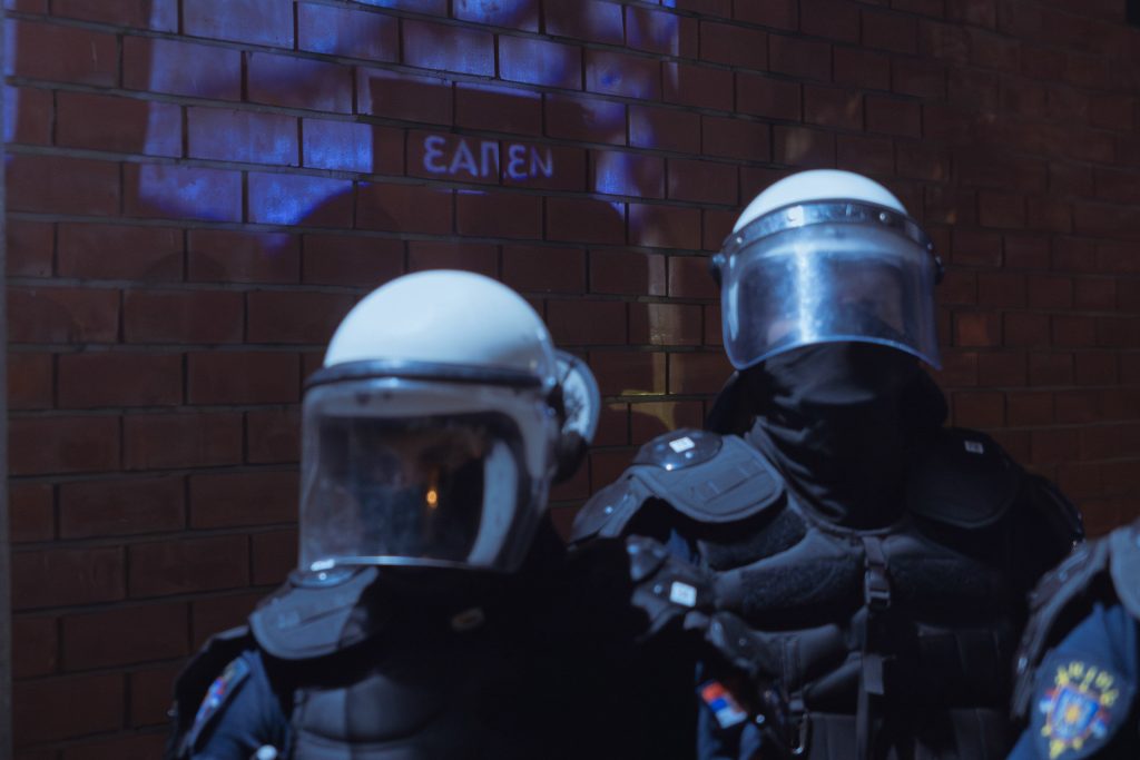 Police officers stand in front of a brick wall with the word 'Exit' faintly visible behind them.