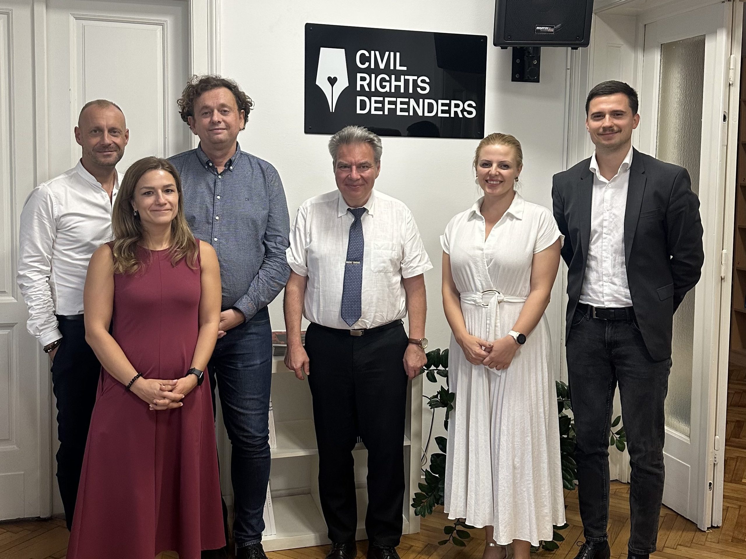 A group of people in business-casual dress standing in front of a sign that reads "Civil Rights Defenders".