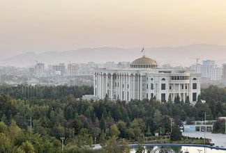 A big white building set amid greenery against a hazy sunrise landscape in Tajikistan
