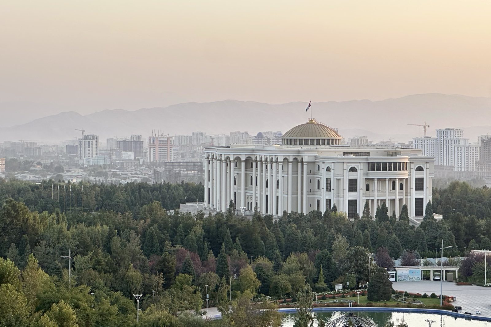 A big white building set amid greenery against a hazy sunrise landscape in Tajikistan
