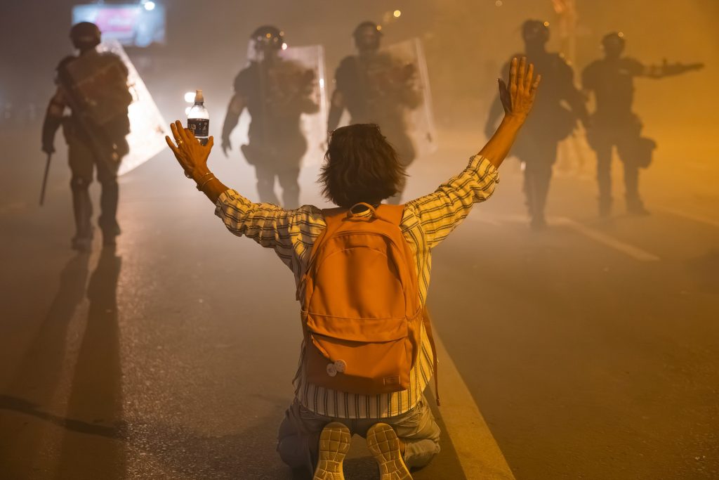 A protester in Serbia kneels in front of an approaching line of police officers.