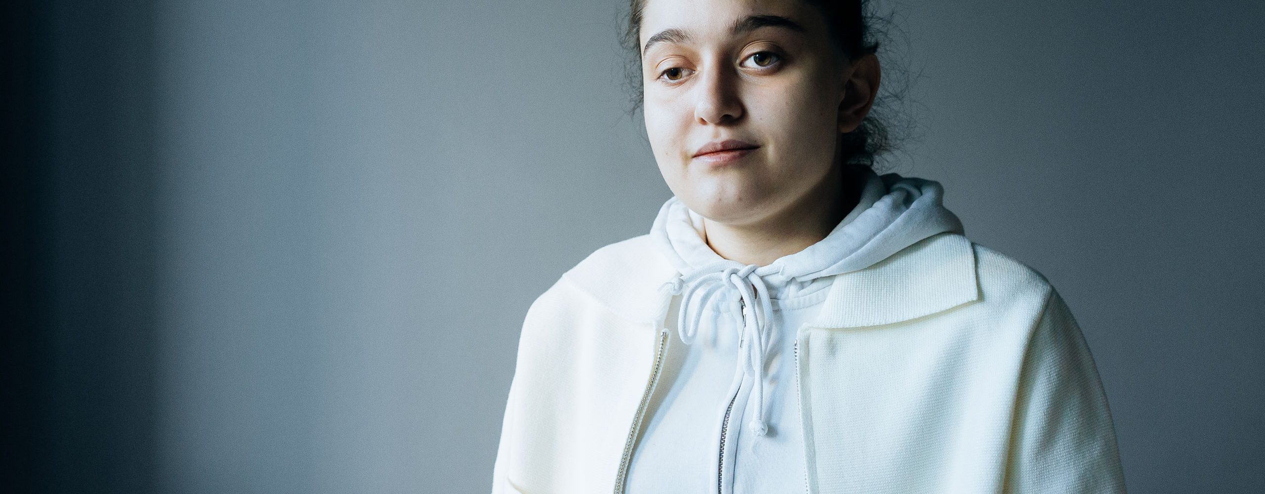 Silvi Aduorian stands against a dark background, looking into the camera with a neutral expression.