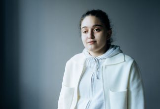Silvi Aduorian stands against a dark background, looking into the camera with a neutral expression.