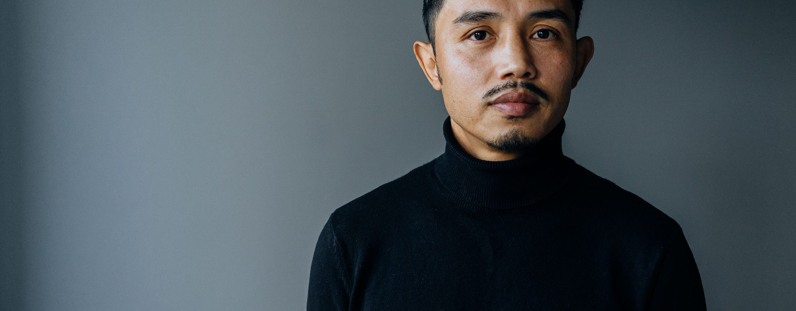 Ali Yusefi stands against a dark background, looking into the camera with a neutral expression.