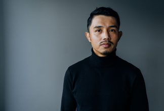 Ali Yusefi stands against a dark background, looking into the camera with a neutral expression.