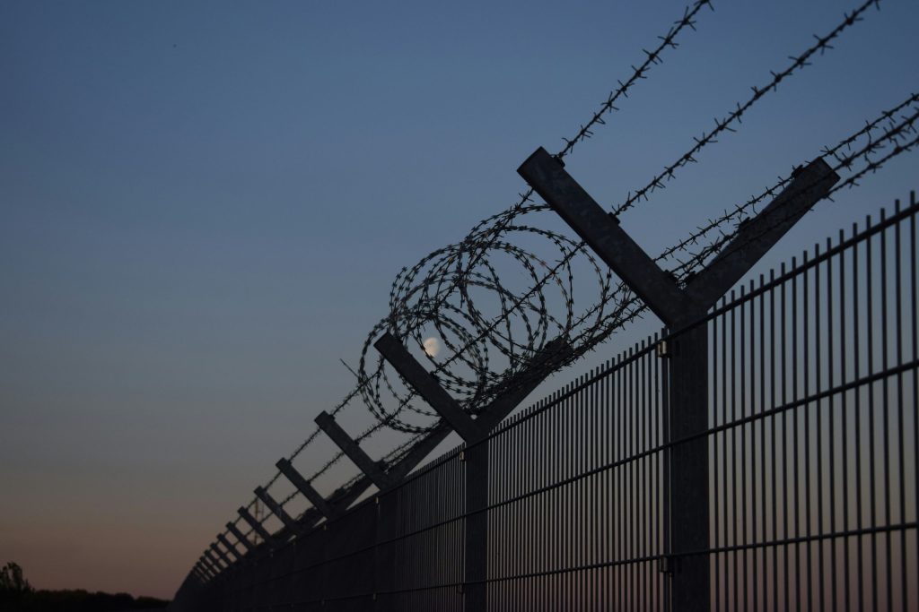 A border with a tall fence with barbed wire during the night.