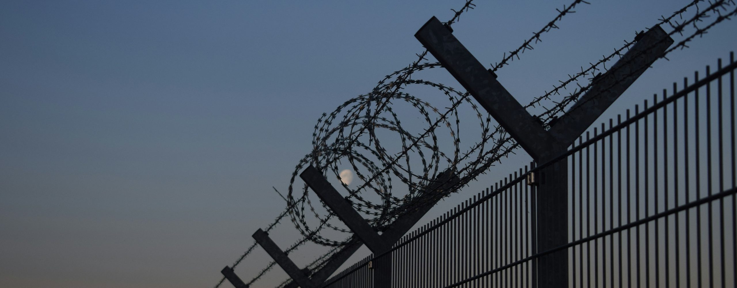 A border with a tall fence with barbed wire during the night.