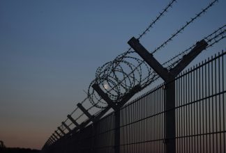 A border with a tall fence with barbed wire during the night.