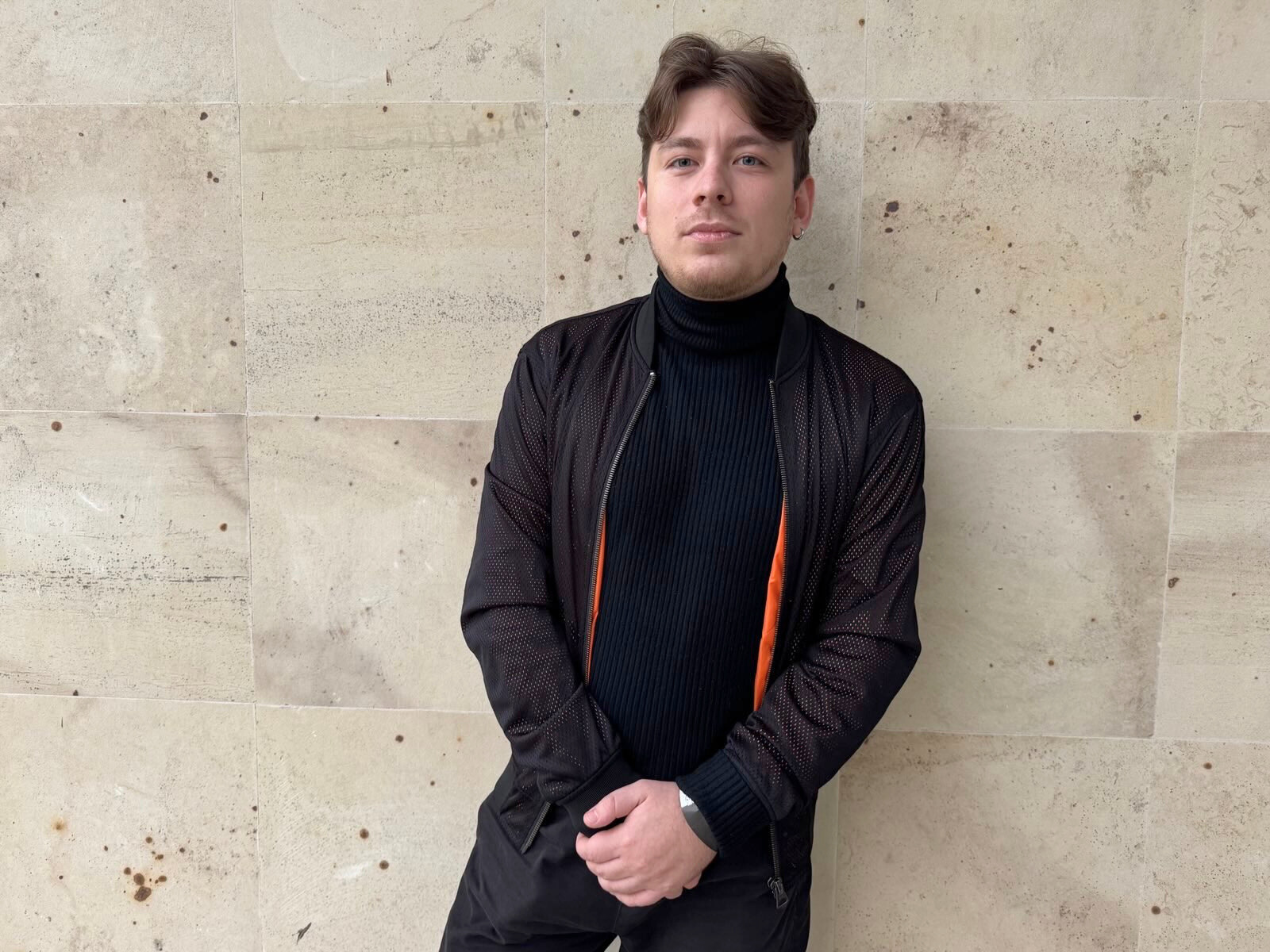 A man dressed in black, standing in front of a wall